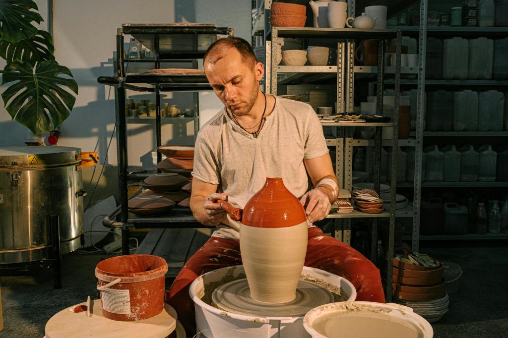 man painting a white pot with orange/clay color