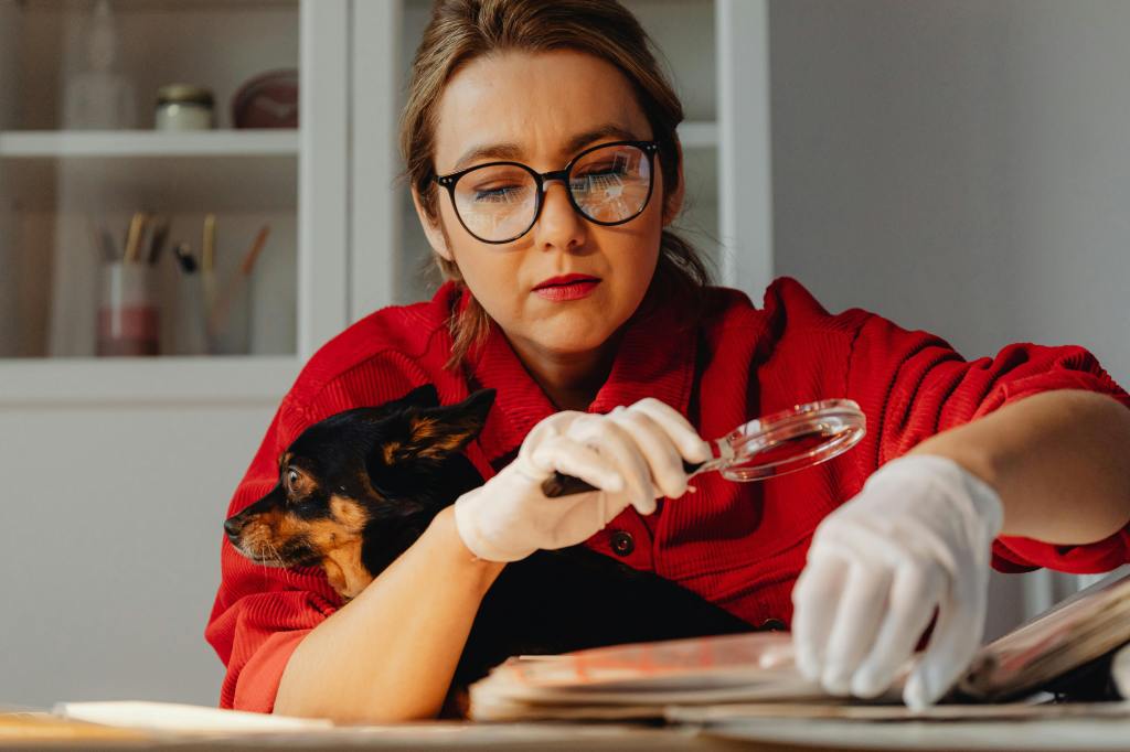 researcher wearing red holding a black-brown chihuahua and looking through a magnifying glass