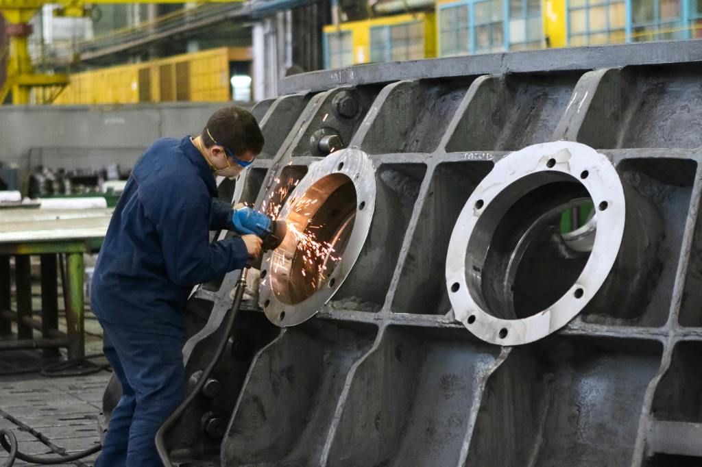 Worker refining a huge metal piece which may be portholes in the side of a ship being built