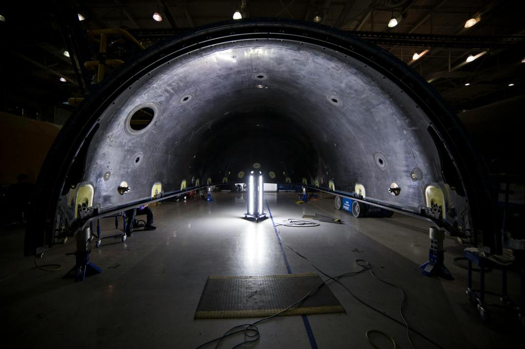 the interior of a large, curved structure, identified as part of a SpaceX Falcon 9 rocket component, possibly a fairing or a section of the main stage. The scene appears to be within a manufacturing or assembly facility, characterized by industrial lighting and equipment.