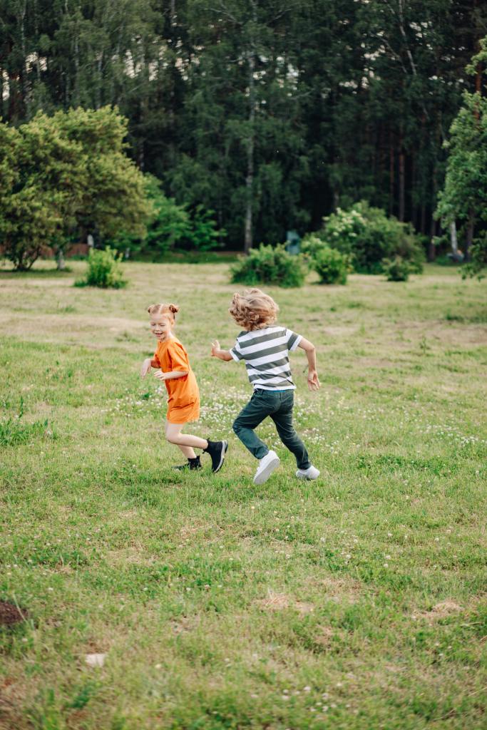 Little kids having fun playing on a green field with large trees in background