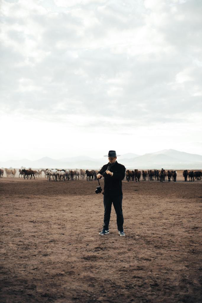 A photographer standing a field with horses in the background