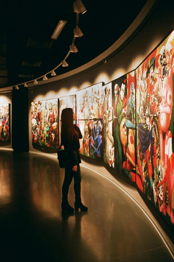 A woman looking at long curved wall full of large floor to ceiling art pieces