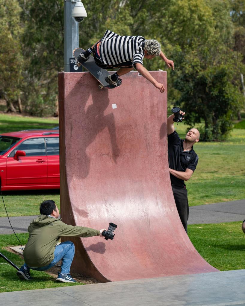 Two photographers filming a skateboarder doing tricks on a half pipe