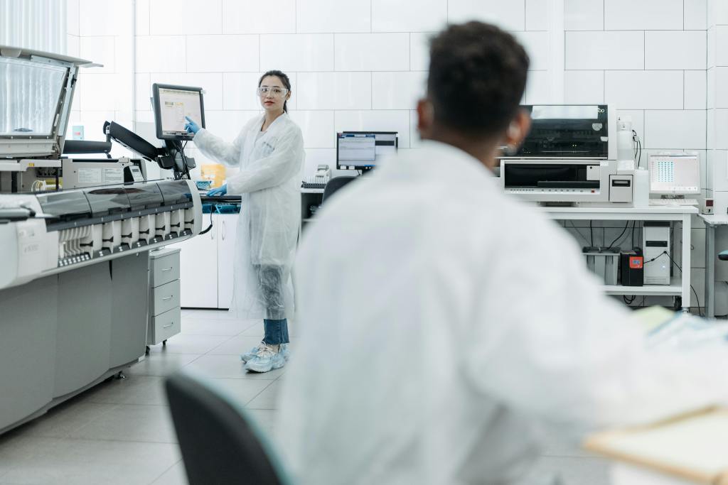 Female scientist or student in lab coat pointing at a screen while looking at her colleague