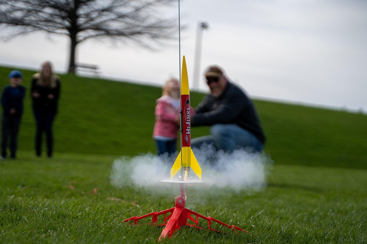 A model rocket launching off grass with people in the background