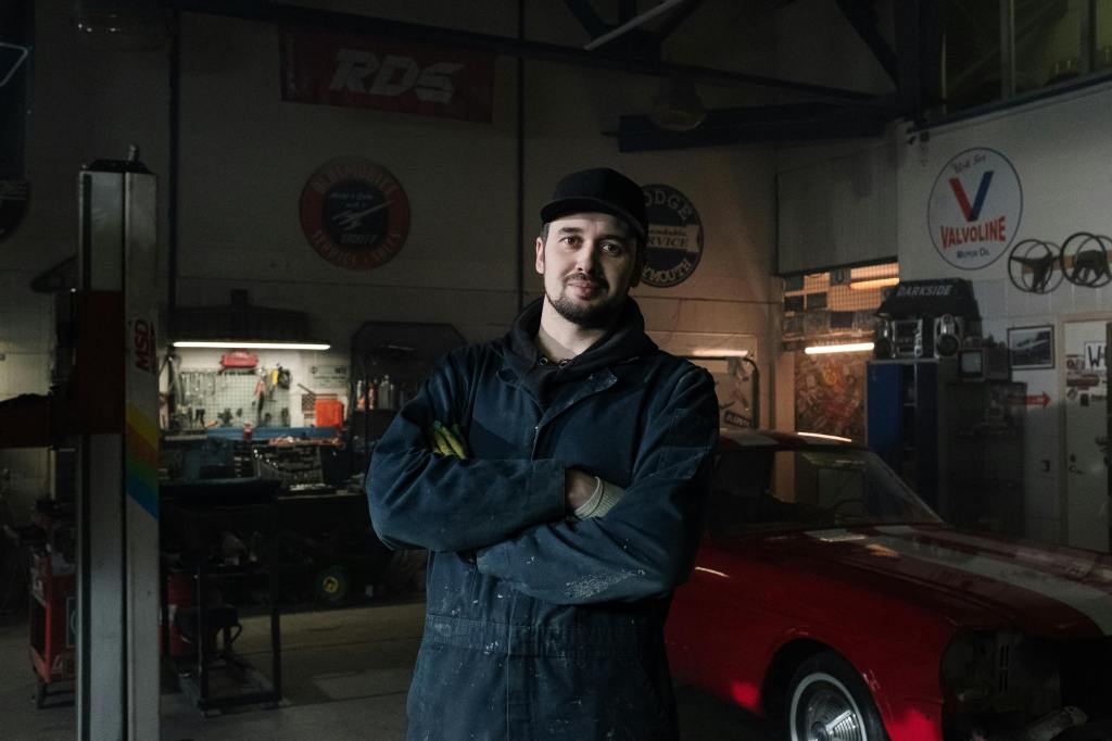 A mechanical engineer standing in garage with a red car behind him