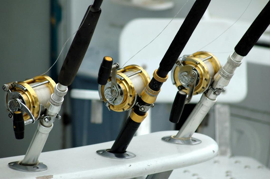 a close-up photograph of three large, gold-colored fishing reels mounted on fishing rods, which are secured in white rod holders on a boat