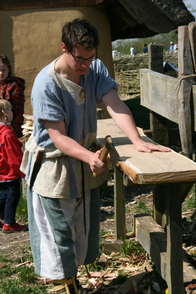 carpenter repairing a big wooden plank appears to be trimming off damaged areas using an axe