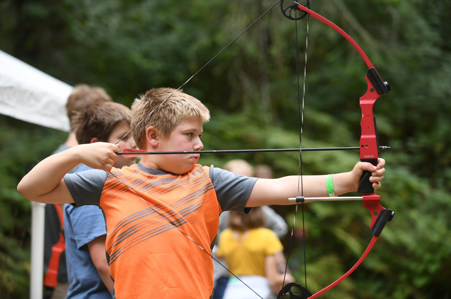 A boy draws back a bowstring with focused aim during an archery activity,