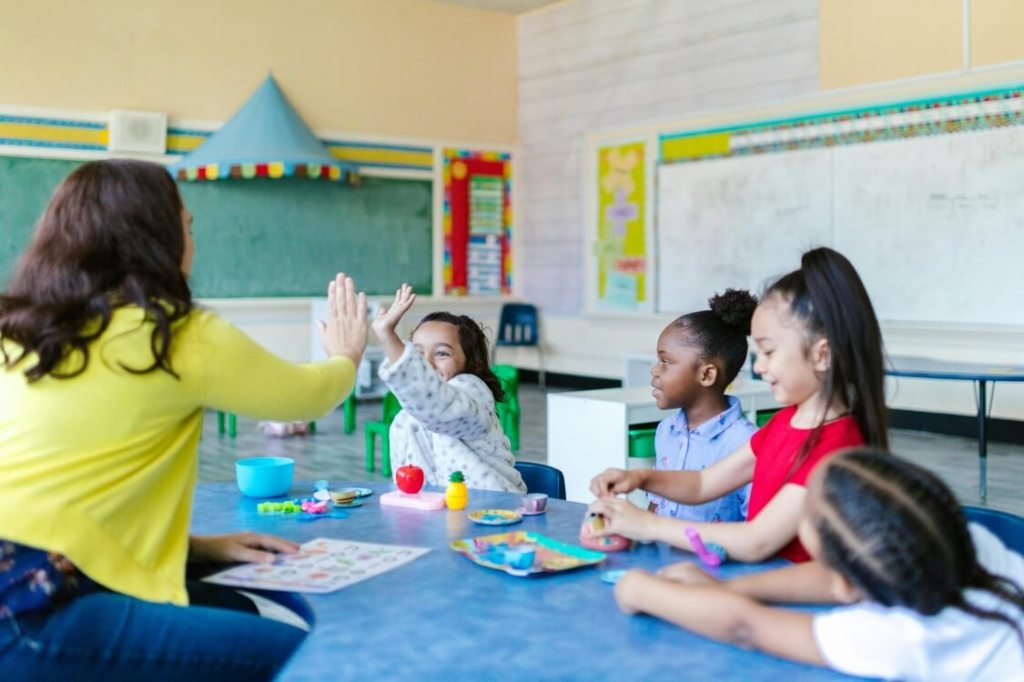 A group of four kids playing with their teacher in a classroom setting.