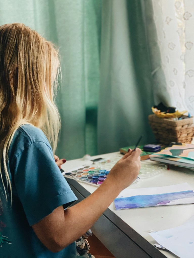 Young woman sits at a desk painting with watercolors