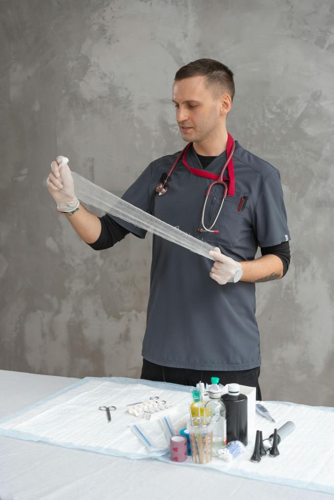 A male veterinary professional in a gray scrub suit and white latex gloves is preparing medical supplies. He is holding a piece of dressing or bandage and examining it.
