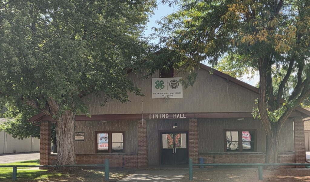 Front view of a building labeled “Dining Hall,” featuring brick columns, large windows, and 4‑H and Colorado State University Extension logos above the entrance, surrounded by tall shade trees.